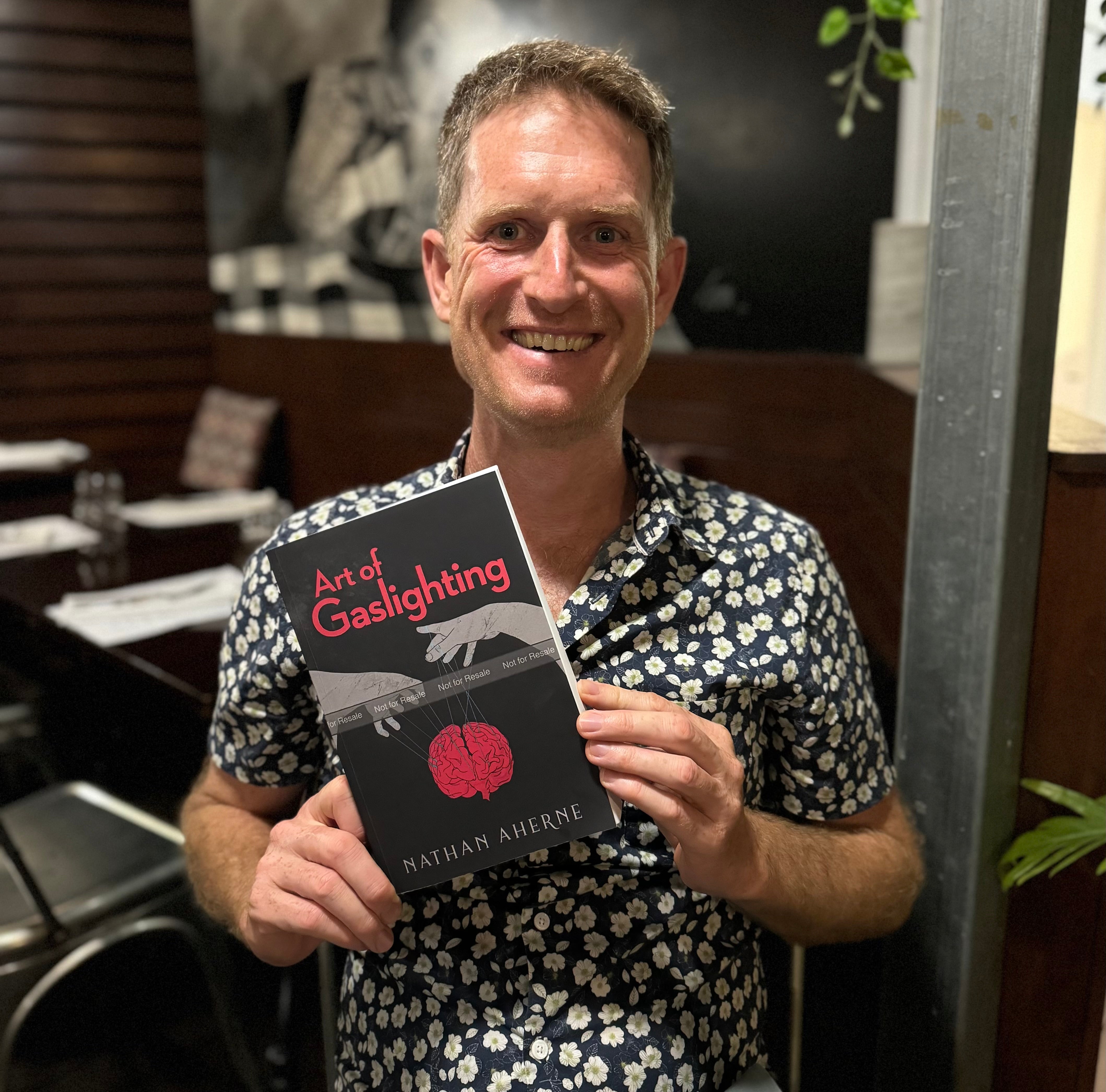 Nathan Aherne holding an author proof of The Art of Gaslighting